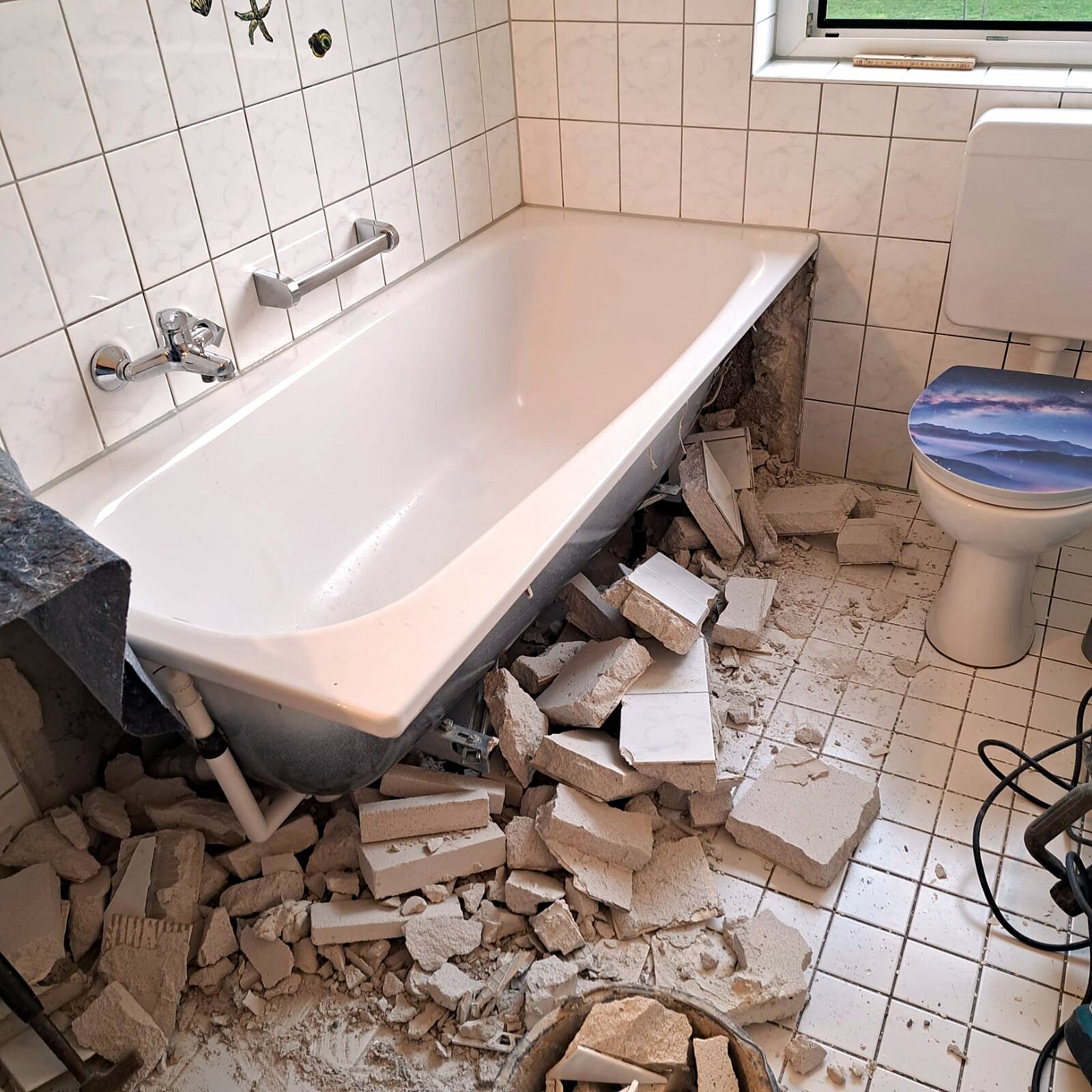 Bad vor der Sanierung mit Badewanne und abgeschlagenen Fliesen